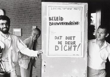 Henk van Gerven (links) en Jo van Dijk (rechts) dragen een verwaarloosde deur binnen in de vergadering van de bouwvereniging.